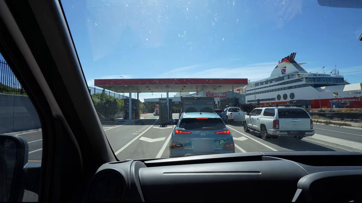 Vehicles queueing at the check-in booths at Geelong, with the ship behind