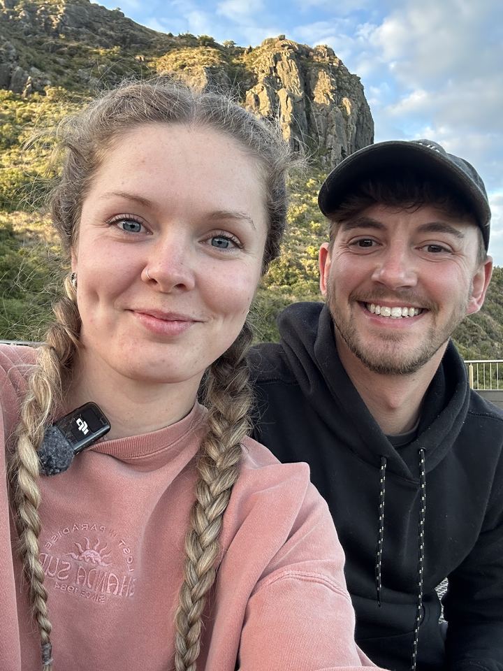 Ashleigh and Luke smiling in a selfie with cliffs behind them in Tasmania
